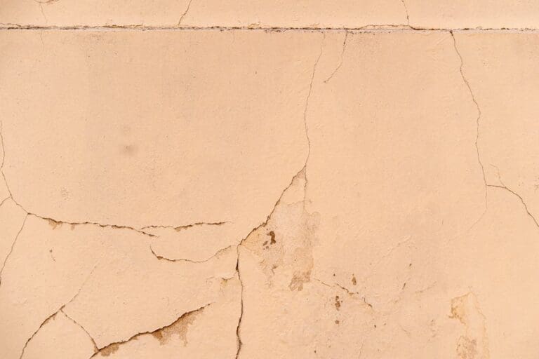 Pęknięcia i łuszczący się tynk na jasnej elewacji domu