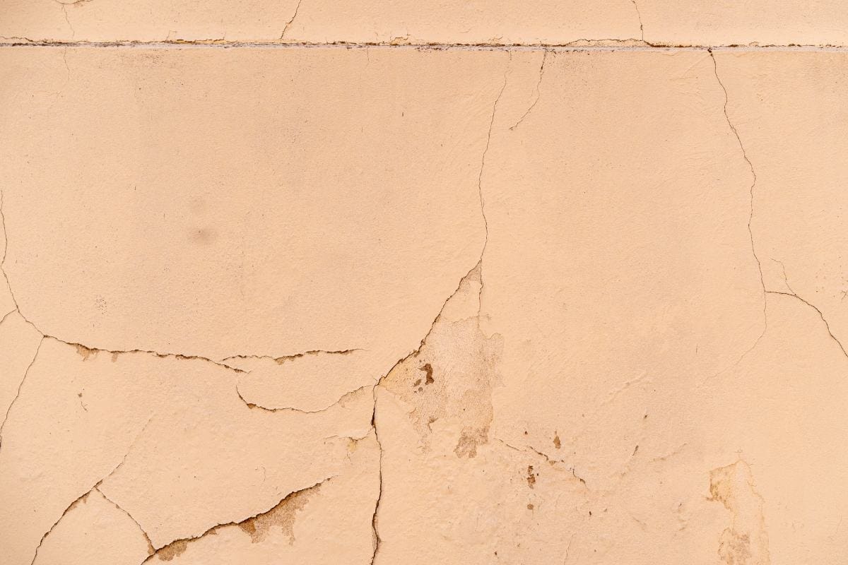 Pęknięcia i łuszczący się tynk na jasnej elewacji domu