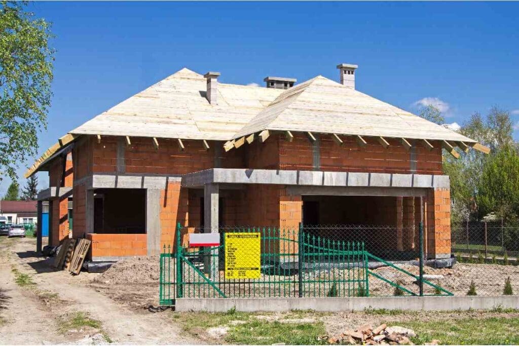 Dom jednorodzinny w stanie surowym z tablicą informacyjną budowy.