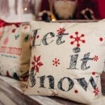 Świąteczne poszewki na poduszki z napisem „Let it snow” na drewnianej ławce, dekoracja w bożonarodzeniowym stylu