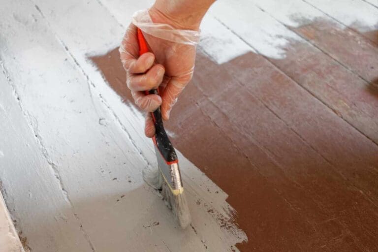 Ręczne malowanie starego parkietu białą farbą podczas renowacji